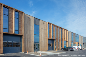 Edificio moderno de Blueprint Automation (PBA) en estilo de madera con varias ventanas grandes y puertas de garaje. Hay coches aparcados delante y un cielo azul en el fondo.