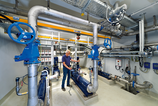 Un empleado maneja un sistema de transporte aéreo con polipasto de cadena y desplaza una carga por una nave industrial