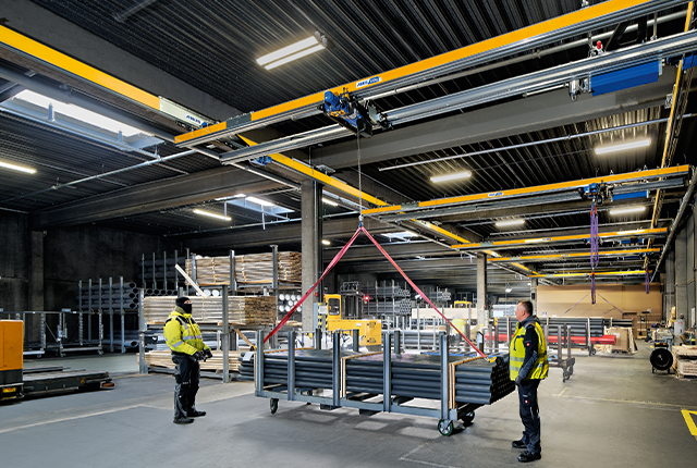 Una grúa de dos vigas ZHB eleva una carga en una nave industrial, mientras los trabajadores supervisan la operación.