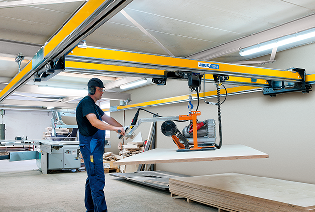 Un trabajador maneja una grúa de dos vigas ZHB-X y eleva una carga con un polipasto de cadena en una nave industrial.