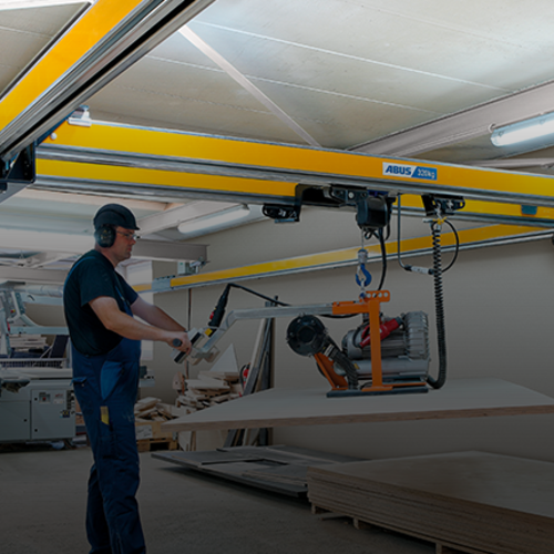 Un trabajador maneja una grúa de dos vigas ZHB-X y eleva una carga con un polipasto de cadena en una nave industrial.