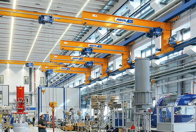 Grúas de pared ABUS en una nave industrial, con una capacidad de carga de hasta 5 t y una luz de hasta 12 m, para el manejo eficiente de varios puestos de trabajo.