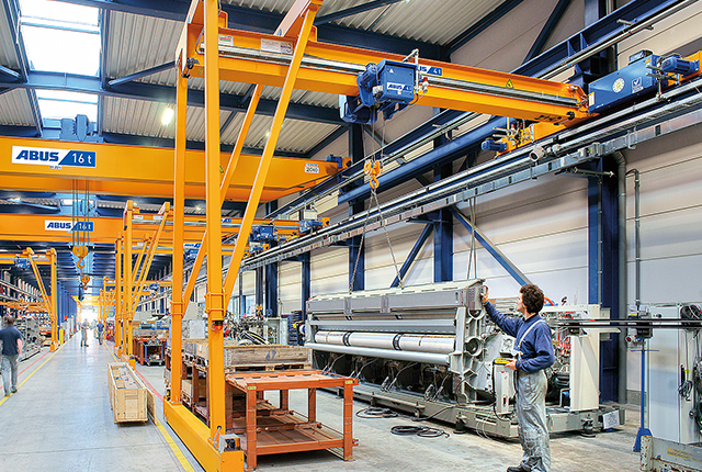 Grúa semipórtico ABUS en una nave industrial con una capacidad de carga de hasta 10 t y una luz de hasta 15 m para la manipulación flexible de materiales en los puestos de trabajo.